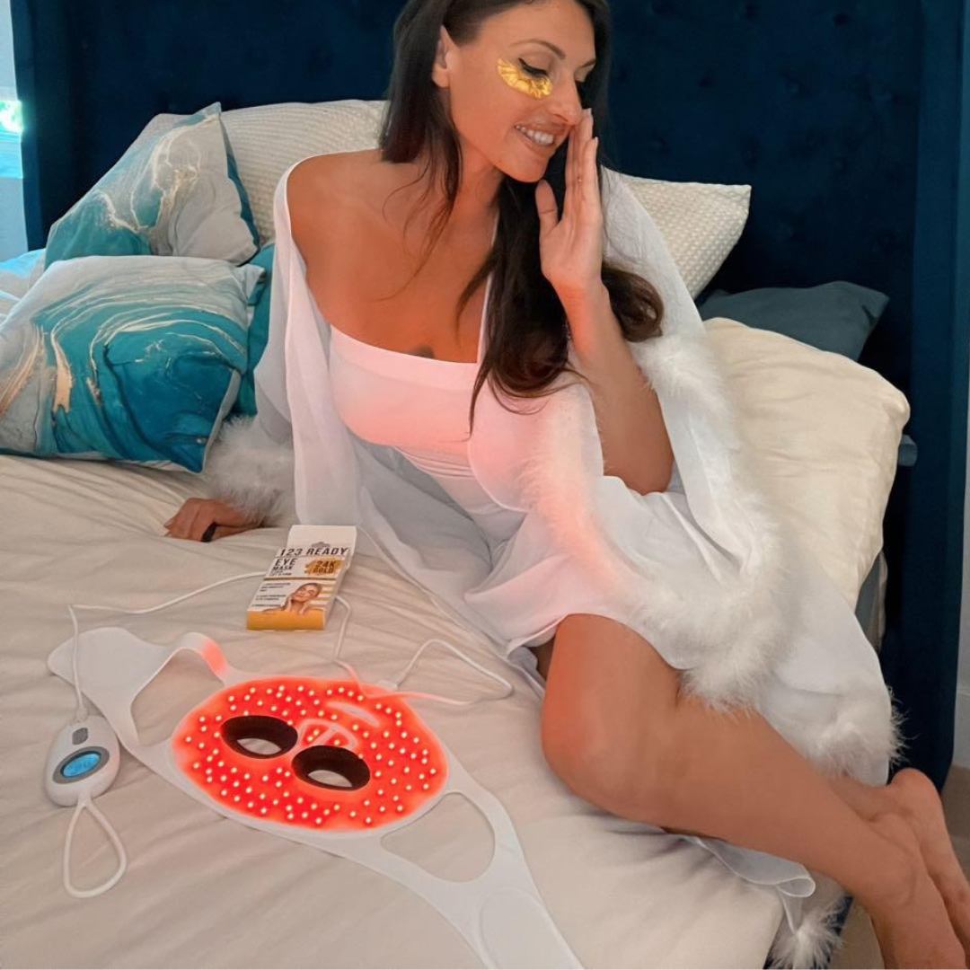 Woman using a red light therapy device on her face in bed