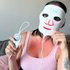 Person wearing a ZAO LED face mask and holding a control device against a neutral background