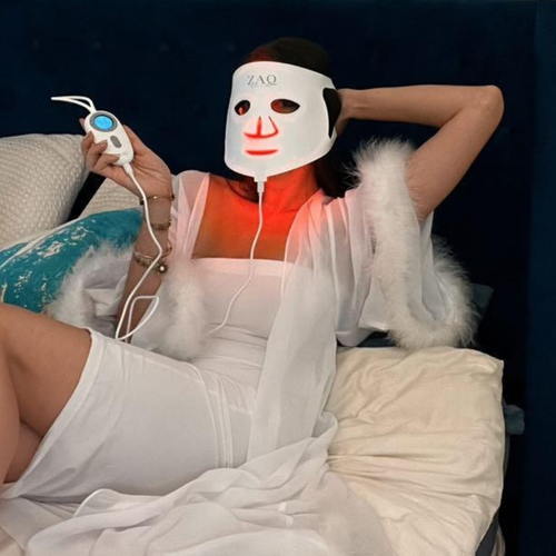 Person wearing a light-up mask with 'ZAQ' branding, lying on a couch.