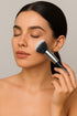 Woman applying makeup with a brush on a neutral background
