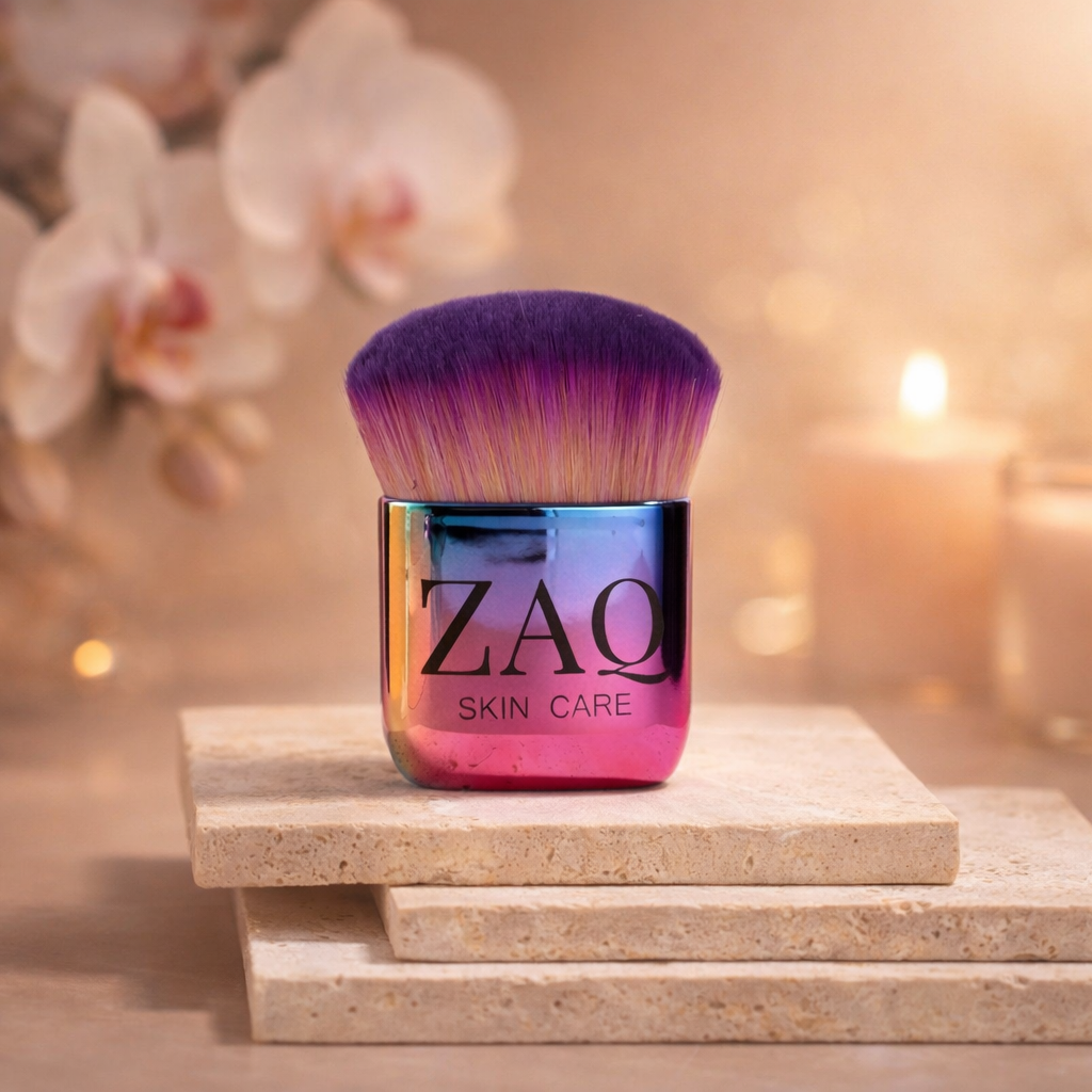 Cosmetic brush with purple and pink bristles on a stack of stones, blurred flowers and candles in the background