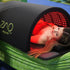 Person lying inside a ZAQ device with red light therapy on a green blanket.
