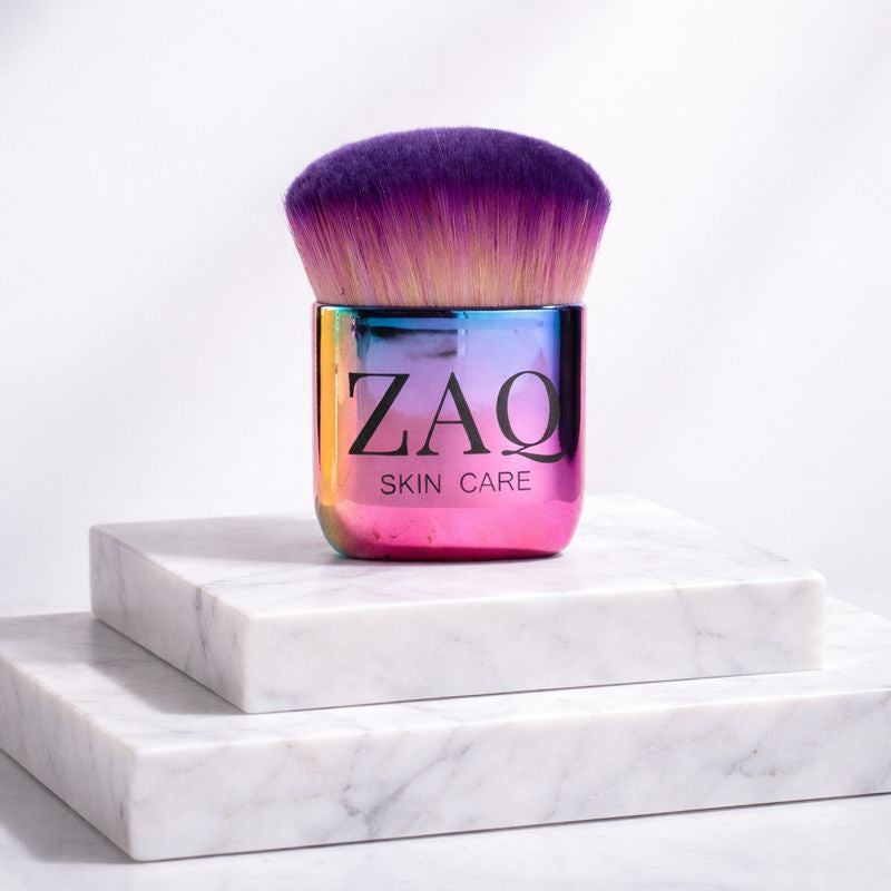 Multicolored makeup brush with 'ZAQ' branding on a white marble surface