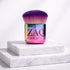 Multicolored makeup brush with 'ZAQ' branding on a white marble surface
