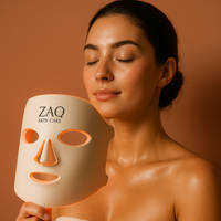 Woman holding a ZAQ Light skincare mask against a brown background