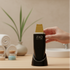 Hand holding a ZAQ skincare device on a wooden surface with towels and a plant in the background