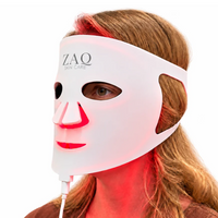 A white ZAQ Skin Care LED light therapy face mask worn by a model, glowing with red light on the skin, against a solid white background.