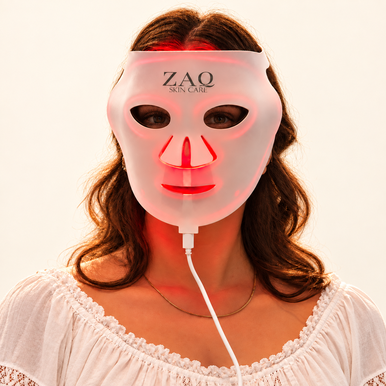 A woman wearing a white ZAQ Skin Care LED light therapy mask that glows with red light, shown against a plain white background.