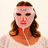 A woman wearing a white ZAQ Skin Care LED light therapy mask that glows with red light, shown against a plain white background.